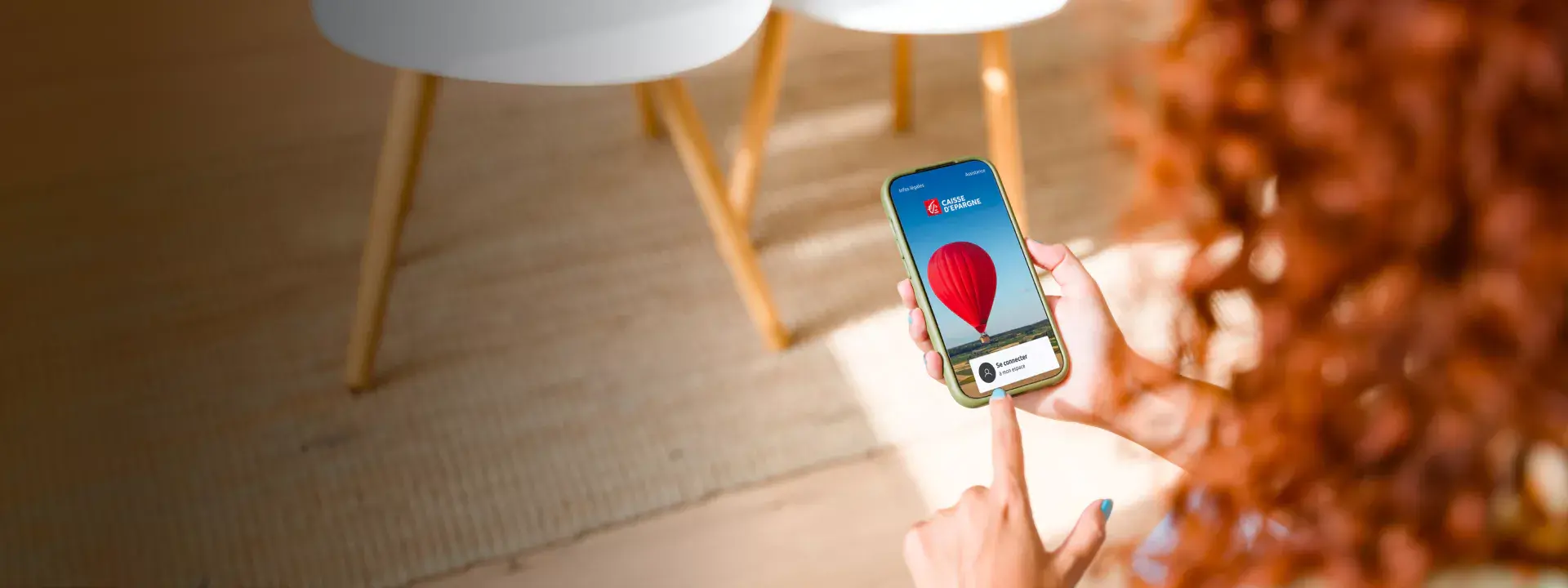 Une personne utilisant un smartphone avec une application affichant un ballon rouge, près d'une table et d'une chaise blanche.